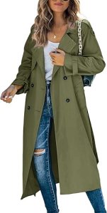 A woman wearing an olive green trench coat, white tank top, and distressed blue jeans, standing outdoors.
