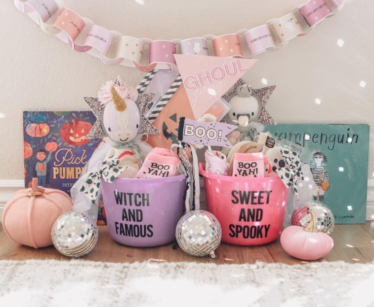 Two coordinated Halloween baskets labeled 'Witch and Famous' and 'Sweet and Spooky' filled with themed treats, plush toys, and decorations, alongside a pastel pumpkin and disco balls.