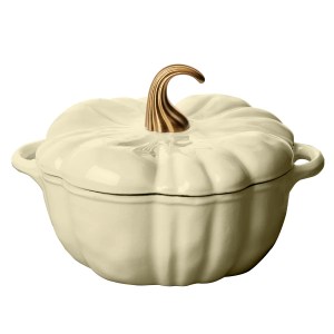 A decorative pumpkin-shaped casserole dish in a creamy white color with a gold stem, perfect for fall-themed dining.