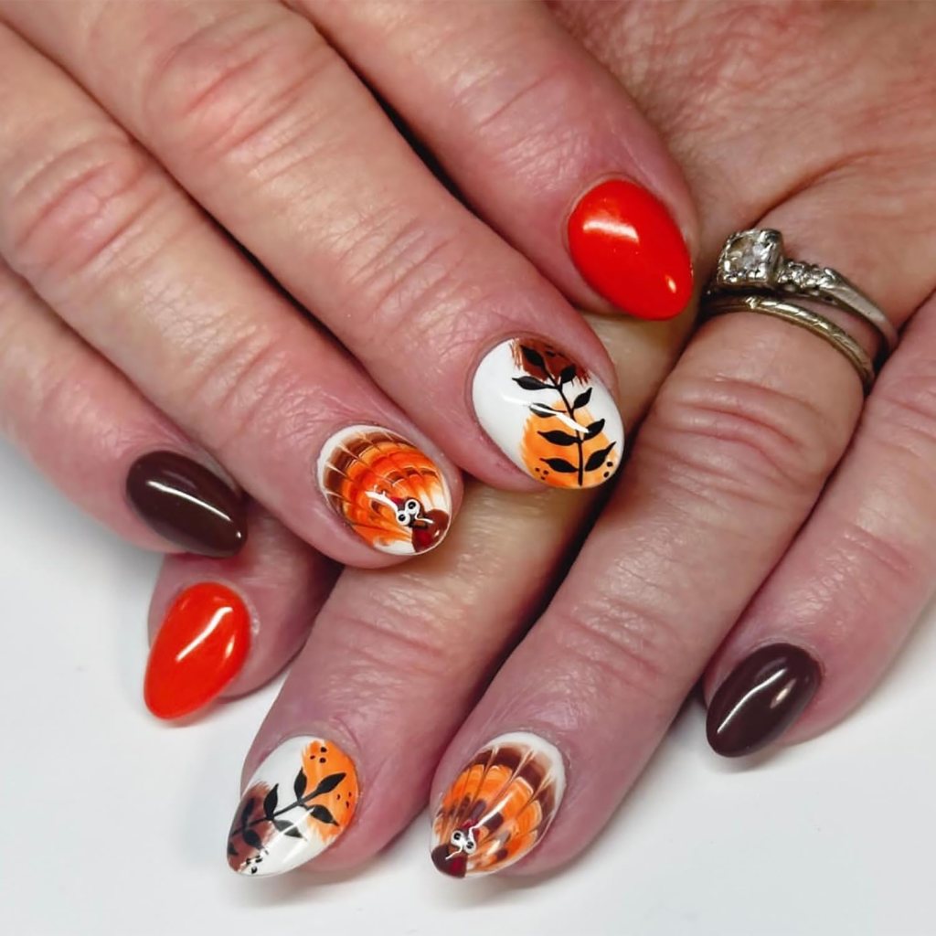 A close-up view of hands with colorful Thanksgiving-themed nails featuring orange, brown, and white polish, decorated with leaf and turkey designs.