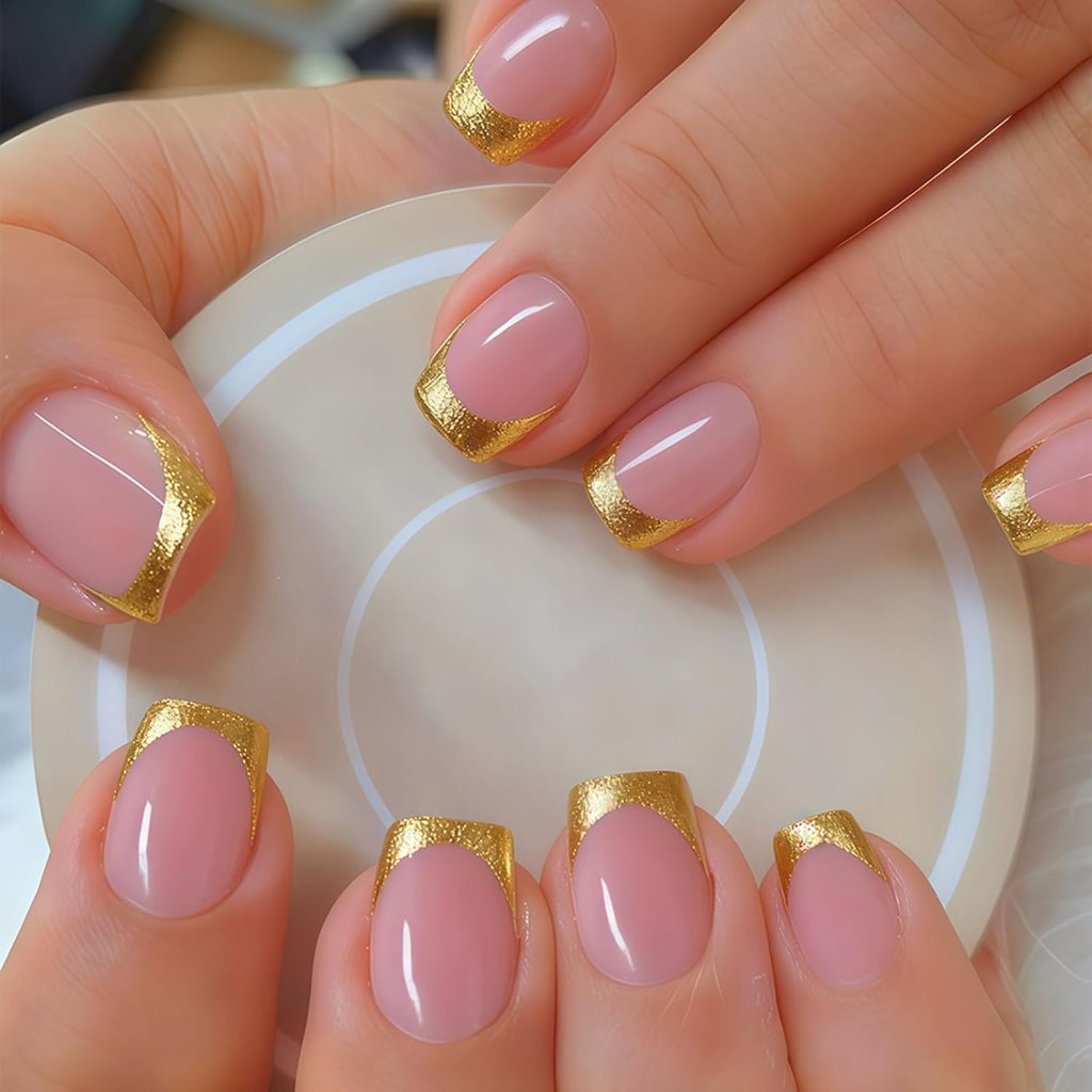 Close-up of well-manicured nails featuring a nude base color with gold French tips.