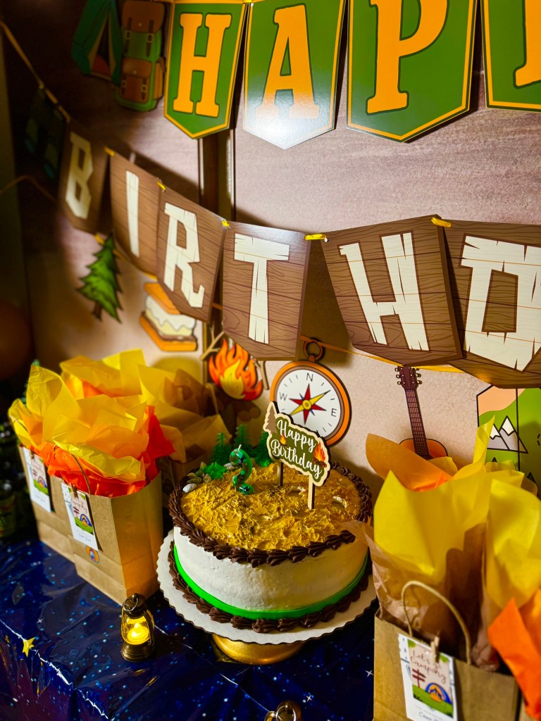 Camping themed birthday cake with trees, rocks, number two candle, and Happy Birthday cake topper.