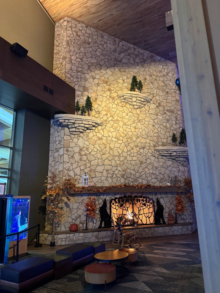 Interior view of the Great Wolf Lodge lobby featuring a large stone fireplace decorated with autumn leaves and pumpkins, along with cozy seating arranged in front.