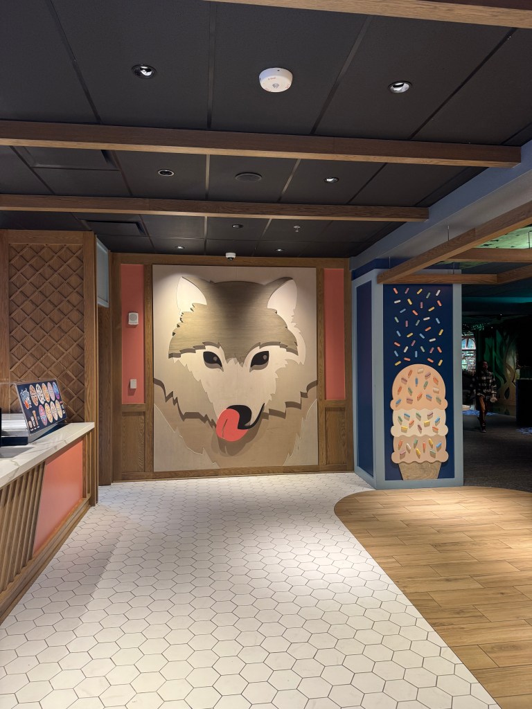 Interior view of Great Wolf Lodge in Grapevine, TX featuring a large wooden wolf mural with a playful expression, surrounded by colorful decor and a well-lit reception area.