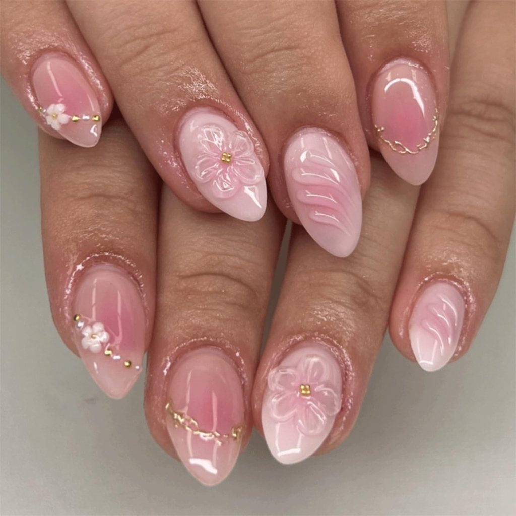 Close-up of manicured nails featuring a pink gradient design with floral accents and gold details.