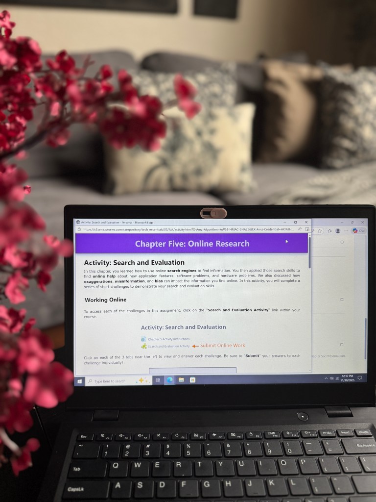 A laptop displaying the 'Chapter Five: Online Research' activity of a tech curriculum, focusing on search and evaluation skills, with a pink flower arrangement in the foreground.