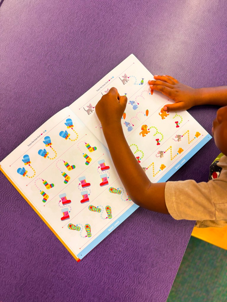 A child coloring in a workbook with colorful illustrations, including animals and various shapes, on a purple table.
