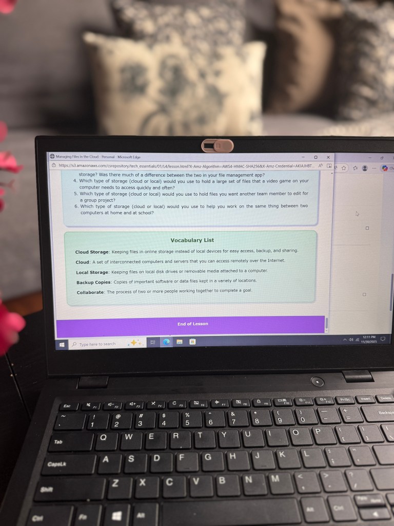 A close-up view of a laptop screen displaying a lesson on managing files in the cloud, featuring a vocabulary list with definitions for cloud storage, local storage, backup copies, and collaboration.