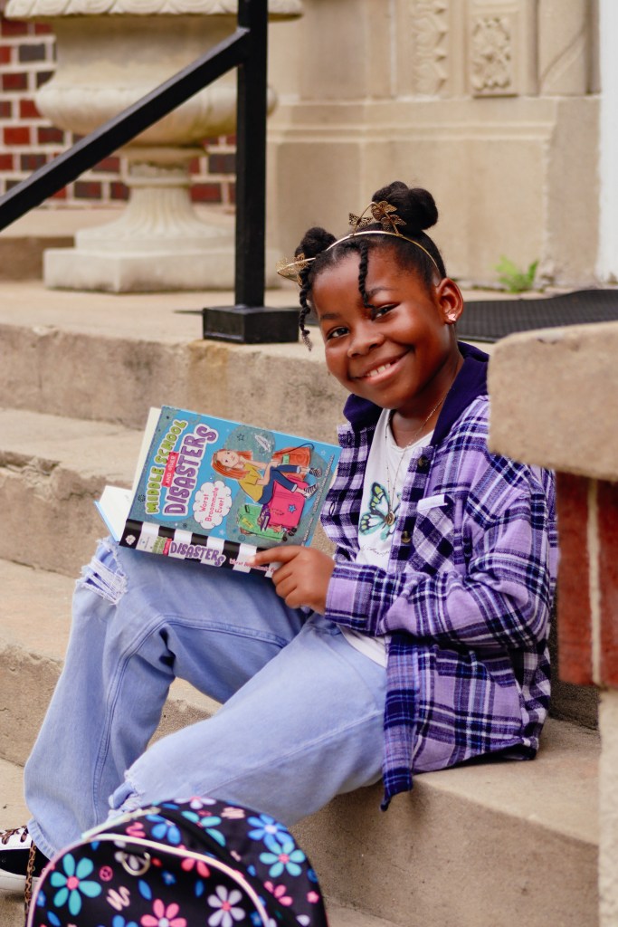 Tween girl holding Middle School and Other Disasters while wearing a backpack before reading.