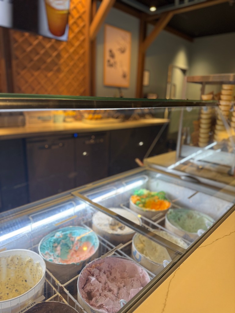 A view of a variety of colorful ice cream tubs in a dessert shop, with wooden accents and a cozy interior.