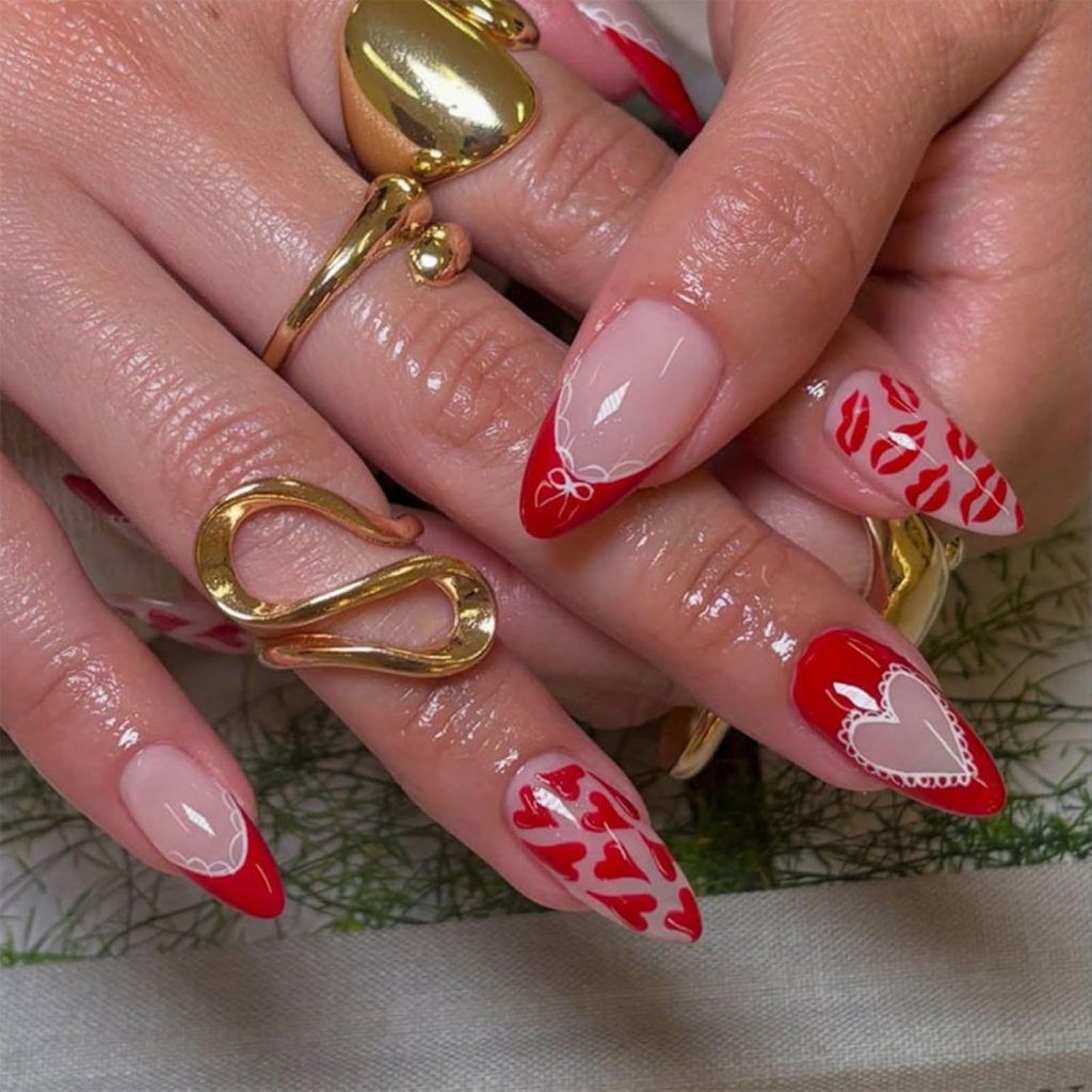 Close-up of manicured hands with red and nude nail designs featuring hearts and lip prints, adorned with gold rings.