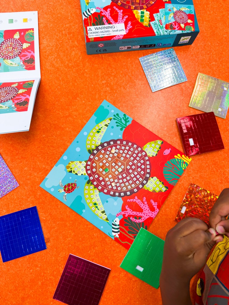 Kindergartner selecting and peeling mosaic stickers for a number matching art project.