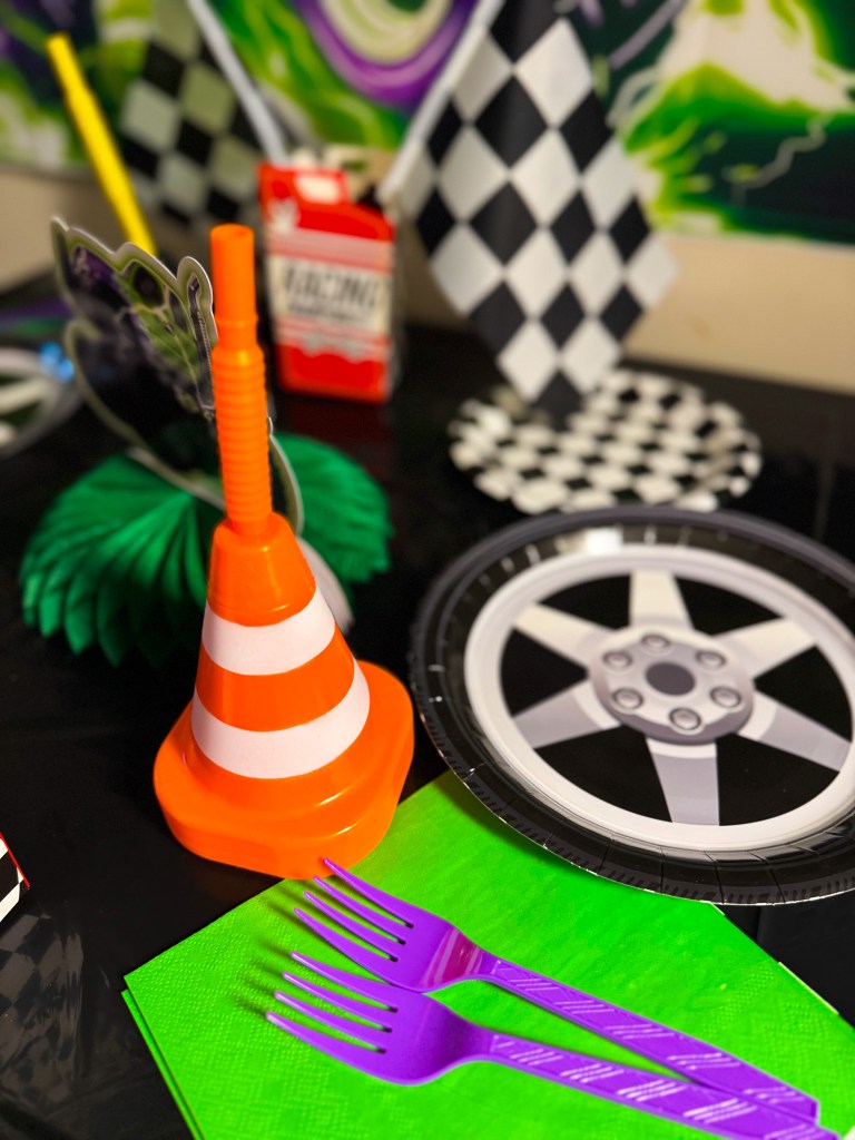 Monster truck birthday party table decorations with traffic cone decor, tire themed plates, checkered racing flags, and colorful party utensils.