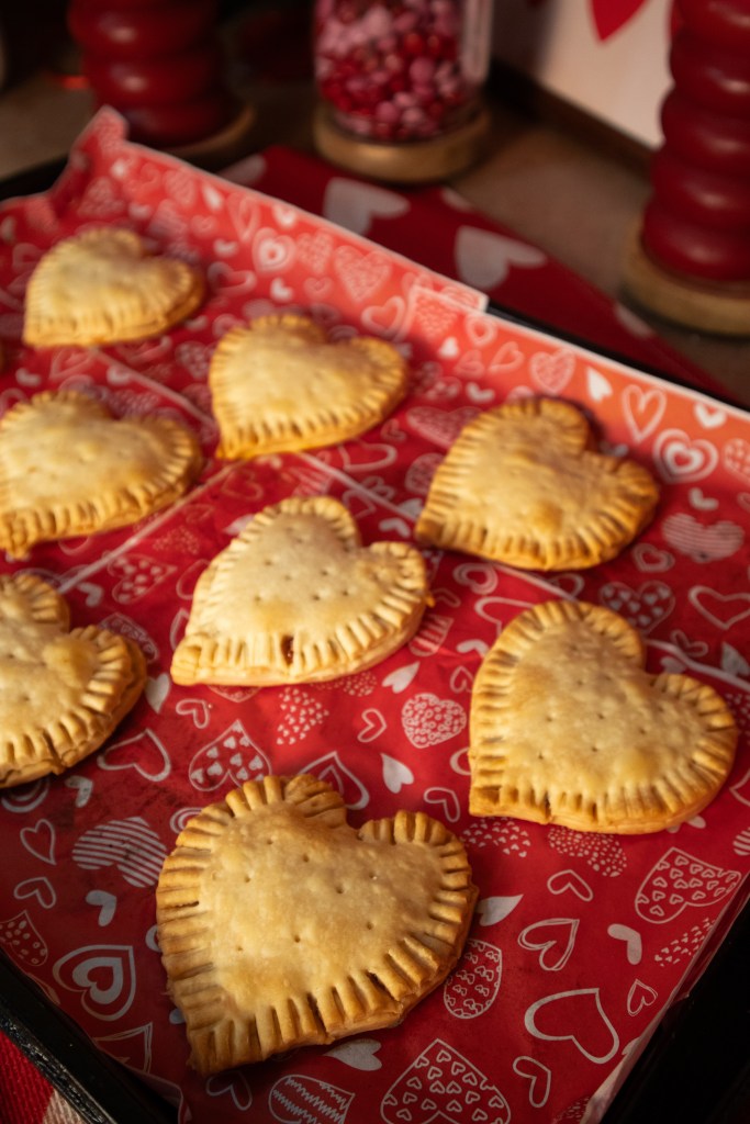 A tray of heart-shaped pastries on red paper featuring heart patterns.