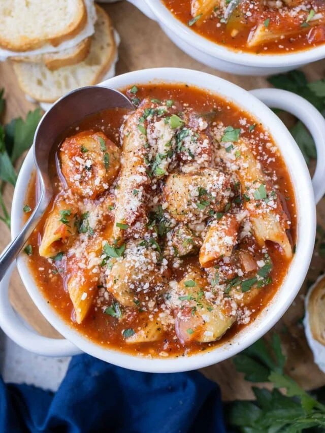 A bowl of Chicken Parmesan Meatball Soup with pasta, meatballs, and a rich tomato broth, garnished with parsley and parmesan cheese.