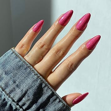 A close-up of a hand with long, pointed nails painted in a shiny pink color, partially covered by a denim jacket.