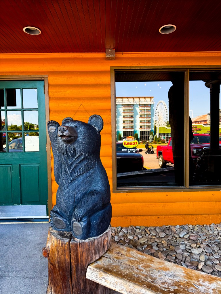 Carved black bear sitting on a wooden stump beside the entrance to Flapjack's Pancake Cabin.