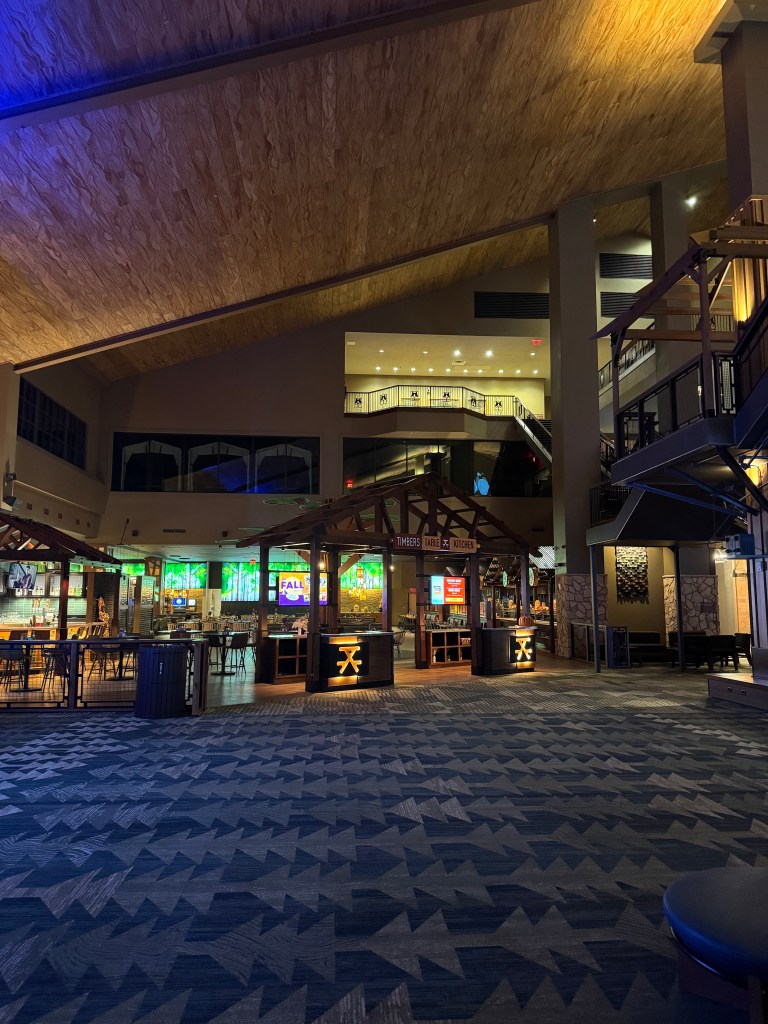 Interior view of Great Wolf Lodge lobby featuring high wooden ceilings, comfortable seating areas, and dining options with vibrant lighting.