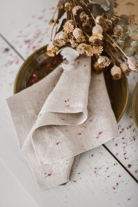 A cozy fall tablescape featuring a textured linen napkin folded elegantly beside a decorative plate, with dried flowers accentuating the natural aesthetic.