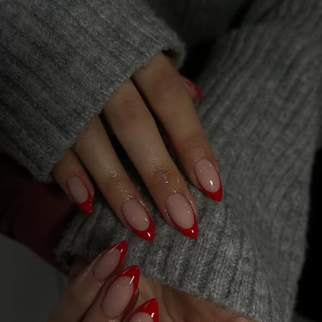 Close-up of hands with stylish nail art featuring nude polish with red tips, resting on a gray knitted sweater.