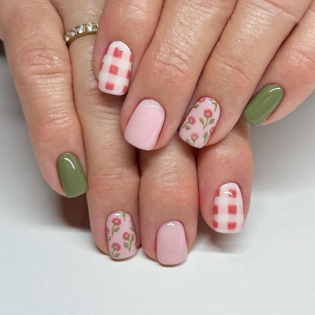 Close-up of manicured hands with colorful nail designs including pink, green, and floral patterns, featuring a red checkered pattern on one nail.