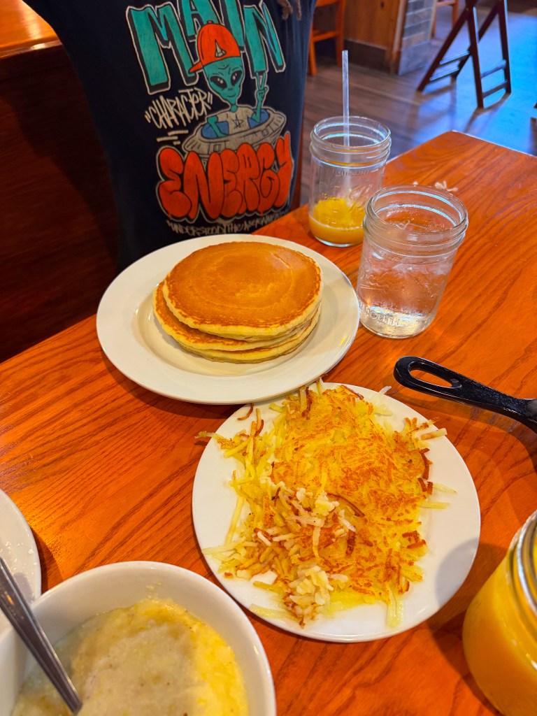 Stack of fluffy golden pancakes served with crispy hash browns and a bowl of creamy Southern grits at Flapjack's.