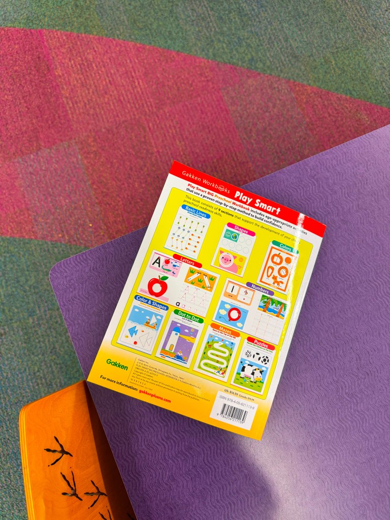 Back cover of the 'Play Smart' Gakken workbook featuring colorful illustrations and educational activities for children, placed on a purple table.