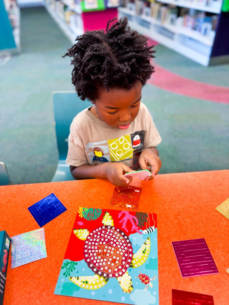 Child carefully peeling mosaic pieces while working on a numbered turtle activity board.
