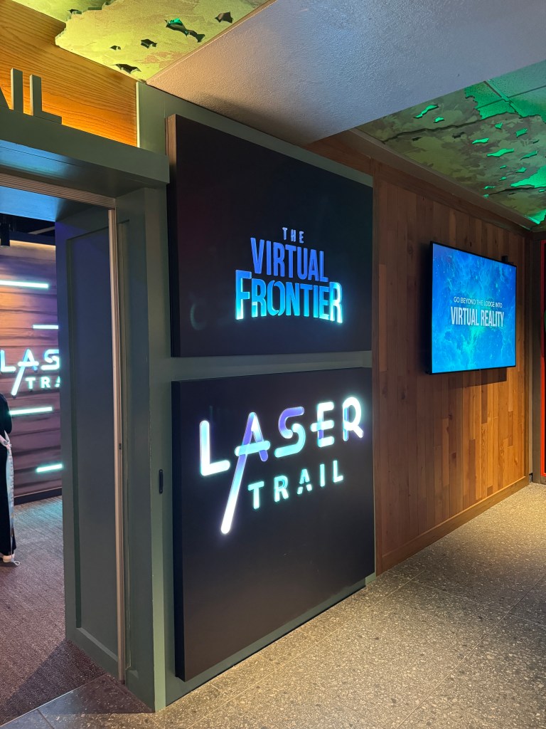 Entrance to the Laser Trail virtual reality attraction at Great Wolf Lodge, featuring illuminated signage and a wooden wall design.