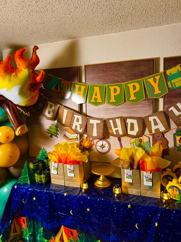 Camping themed happy birthday banner with woodland details, tent graphics, bear, lantern, and campfire decorations.