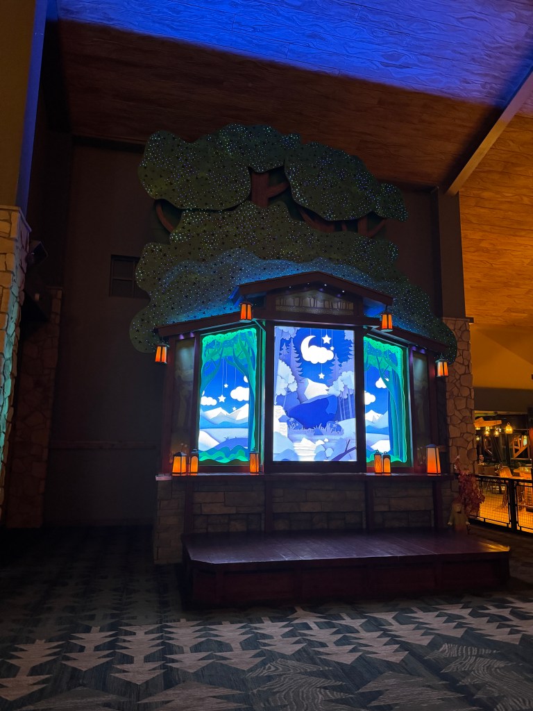 Decorative lobby display at Great Wolf Lodge in Grapevine, TX - featuring a large tree and colorful stained glass style windows depicting a serene landscape, illuminated by ambient lighting.