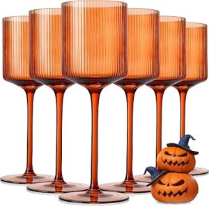 Six elegant amber wine glasses with ribbed design, accompanied by two small pumpkin decorations.