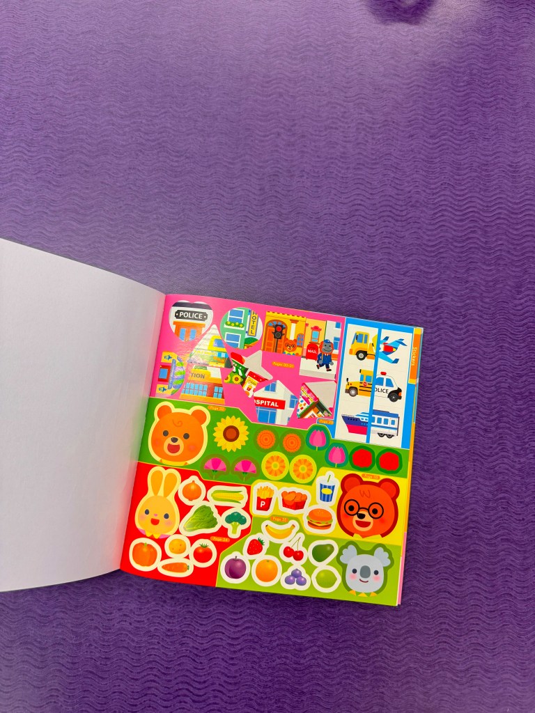 A close-up view of an open sticker book featuring colorful stickers, including animals, fruits, vehicles, and various playful designs on a purple background.
