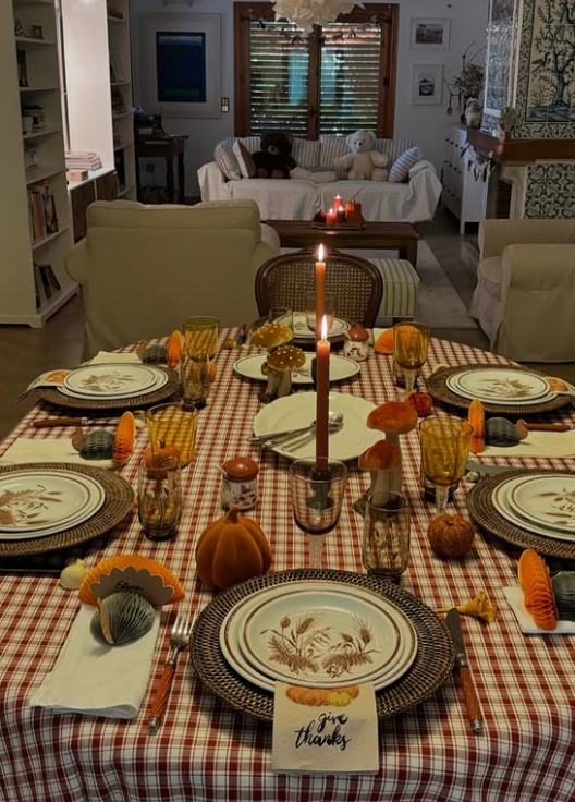 Thanksgiving table settings featuring a red plaid tablecloth, brown dishware, and festive autumn decorations including mini pumpkins and decorative mushrooms, with a cozy living room in the background.