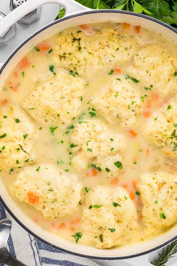A pot of creamy chicken and dumpling soup with fluffy dumplings and colorful carrots, garnished with fresh herbs.