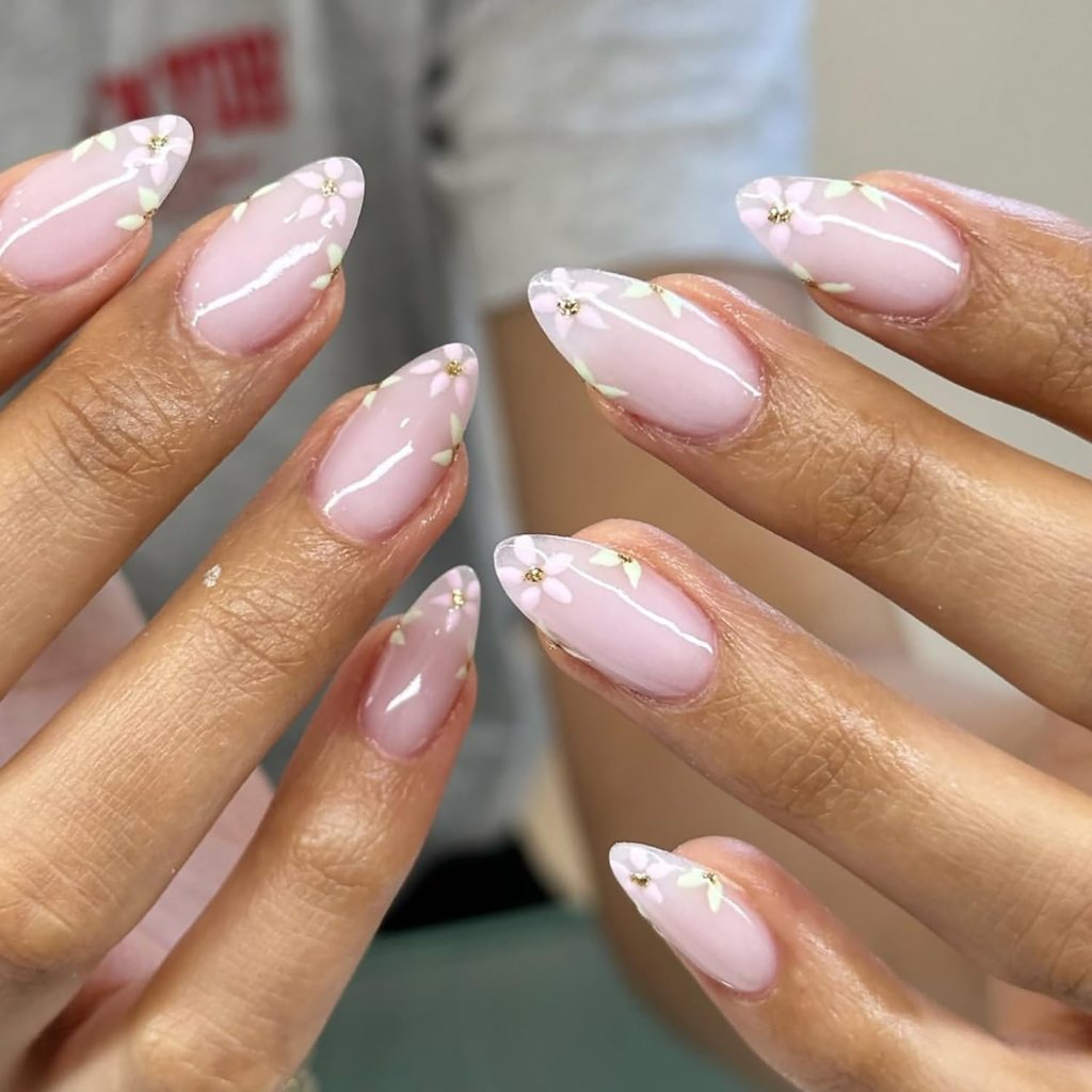 Close-up of hands showcasing stylish, pointed pink nails decorated with white floral accents and glossy finish.