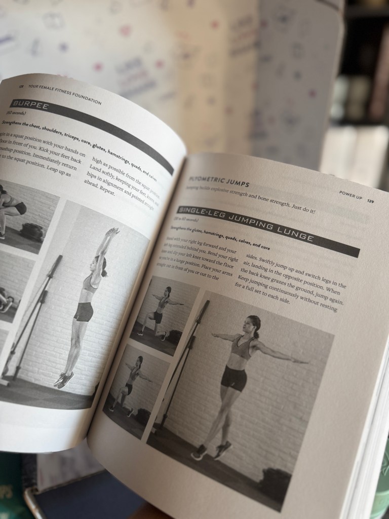 A close-up shot of an open fitness book displaying exercises, including burpees and single-leg jumping lunges, with illustrations demonstrating the movements.